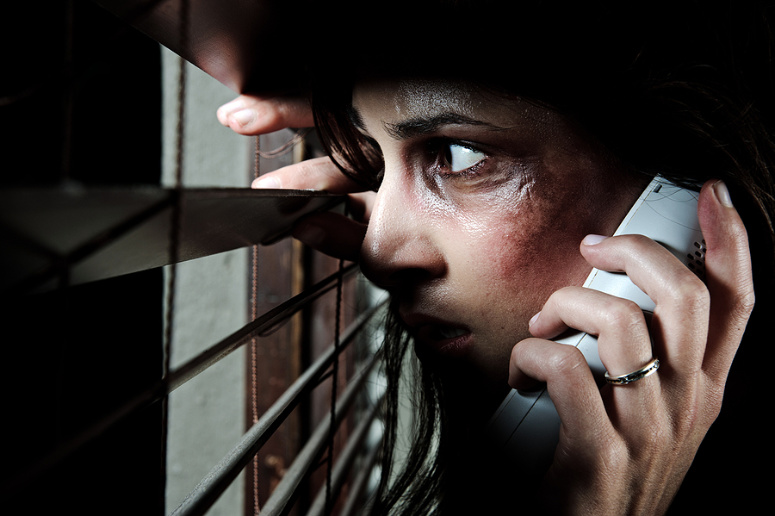 Woman peeking through blinds with fear.