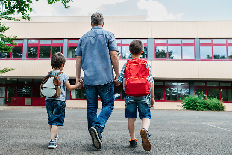 A photo of a father walking his kids to school