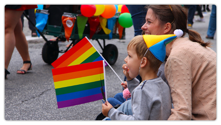 August 20, 2016: Young woman with child holding rainbow flags at gay Pride Parade.